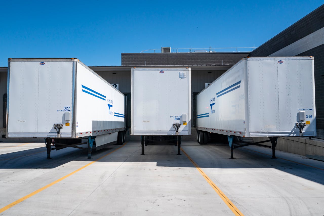 team-02 Three white cargo trailers parked at an industrial shipping dock under clear blue skies.